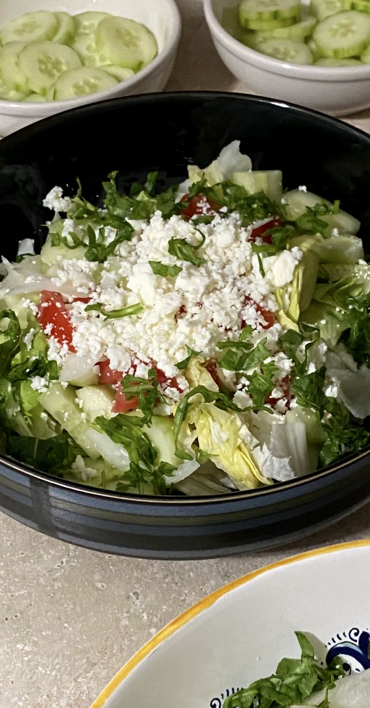 Greek salad with crumbled feta and chopped greens in a black bowl