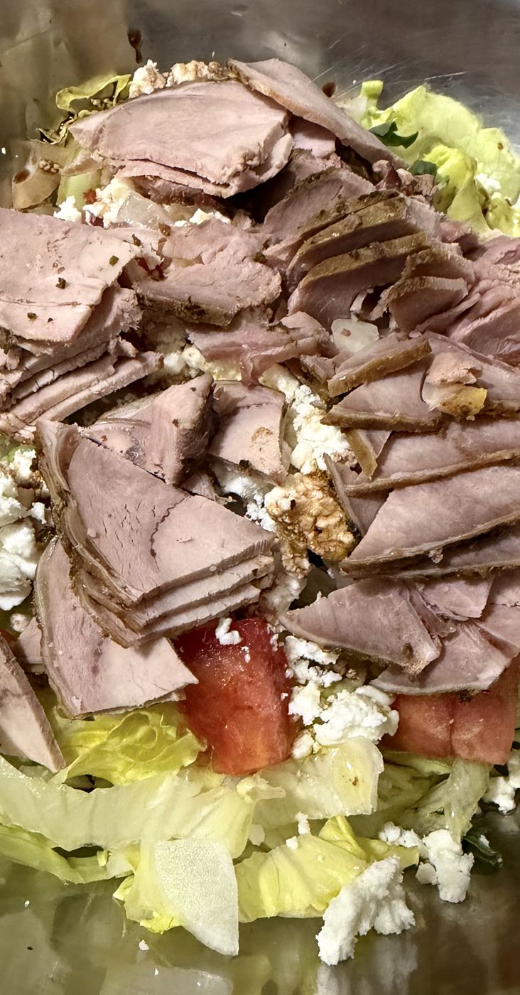Roast beef salad over crisp lettuce with tomato and feta, in a steel mixing bowl