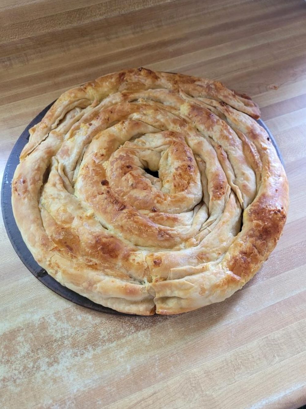 A golden coiled filo pie, fresh out of the oven on a wooden counter